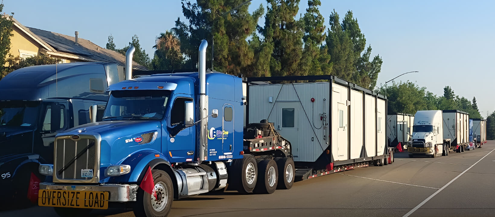 Fleet of Elitone Transportation trucks hauling multiple oversized modular buildings on a suburban street.
