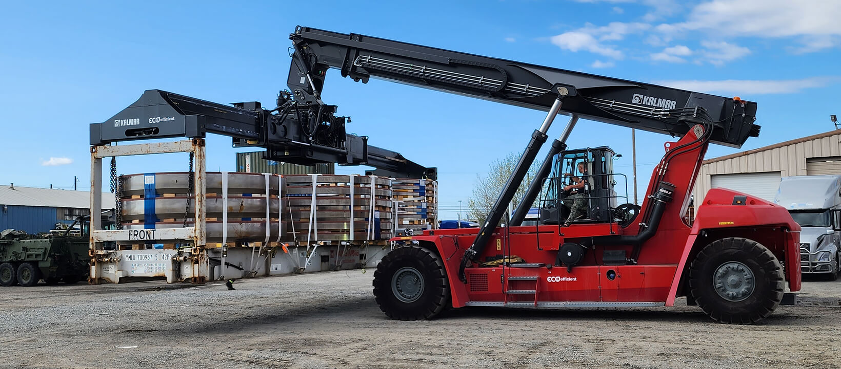 Red Kalmar reach stacker lifting a steel coil container at Elitone Transportation facility.