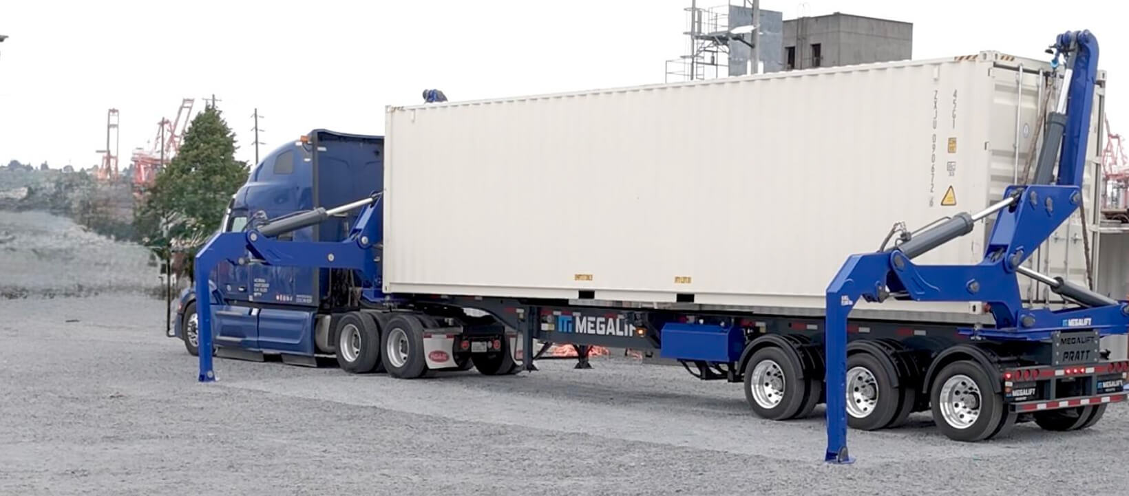 Blue truck with Megalift system lifting a white shipping container at a logistics yard.